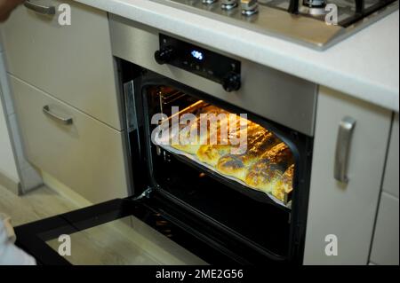 la tarte maison est préparée et cuite dans un plat spécial dans un four électrique dans la cuisine. Vue du gâteau chaud fini avec la porte du four ouverte. Une délicieuse pâte aux pommes saupoudrée de pavot Banque D'Images