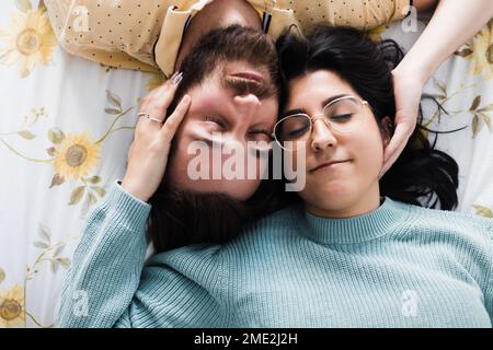 Vue de dessus d'un jeune couple ravi avec des yeux fermés allongé sur un lit confortable et touchant la face l'un de l'autre tout en se reposant ensemble pendant le week-end Banque D'Images