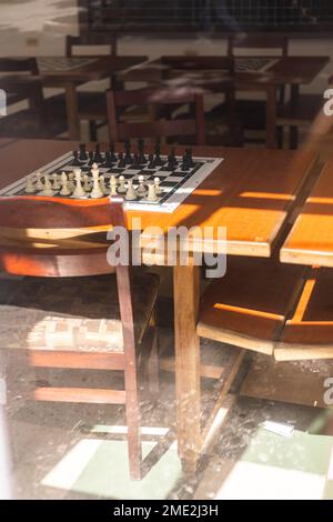 Vue à grand angle à travers la fenêtre de vieilles tables en bois avec jeu d'échecs dans la lumière du soleil Banque D'Images