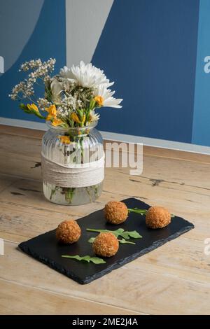 De dessus des boules de fromage appétissantes servies sur tableau noir près vase transparent avec fleurs en fleur Banque D'Images