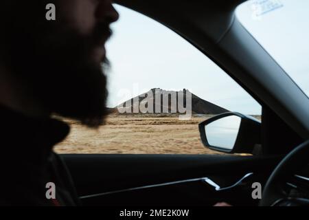 Vue latérale de la récolte, homme voyageur méconnaissable conduisant une voiture lors d'un voyage dans la campagne en Islande Banque D'Images