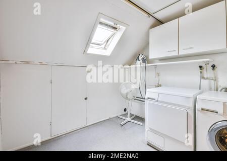 Intérieur moderne et lumineux buanderie avec lave-linge et sèche-linge, ventilateur et armoires Banque D'Images