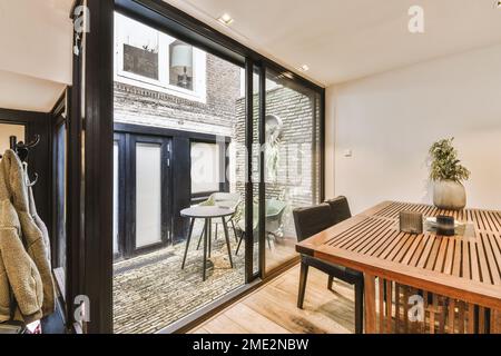 Intérieur de l'appartement moderne avec salle à manger près des portes en verre à la petite terrasse avec chaises et petite table ronde Banque D'Images