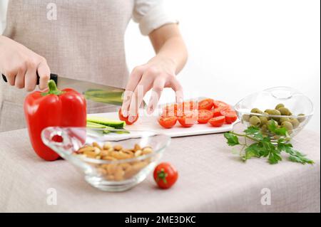 Concept de régime alimentaire sain. Vue en grand angle des mains de femmes coupant concombre dans la cuisine côté droit tomates en tranches laitue sur le côté gauche concombres tableau en porcelaine blanche manucure douce jeune main femelle Banque D'Images