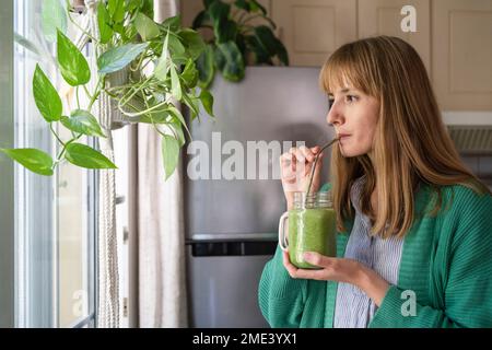 Femme buvant du smoothie vert à la maison Banque D'Images