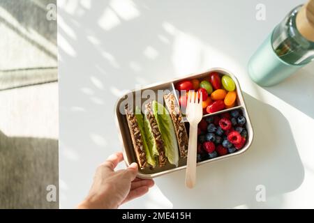 Main de la femme tenant la boîte à lunch avec des aliments sains sur la table Banque D'Images