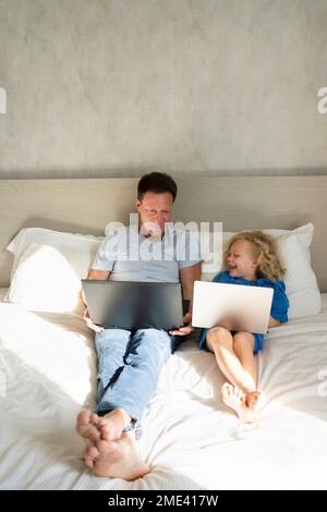 Fille et père heureux avec des ordinateurs portables sur le lit dans la chambre Banque D'Images