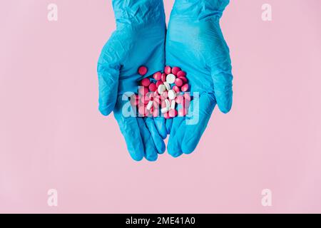 Mains dans des gants médicaux avec des pilules. Fond rose. Concept médical, vue de dessus, espace pour le texte Banque D'Images