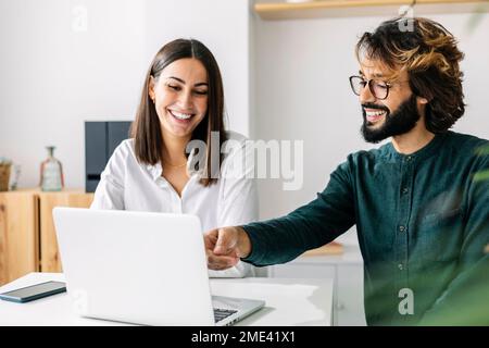 Un homme d'affaires heureux discutant avec un collègue sur un ordinateur portable sur son lieu de travail Banque D'Images