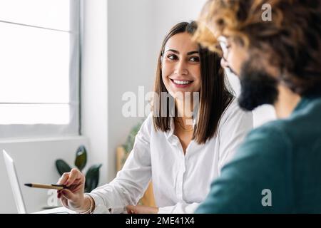 Un travailleur indépendant souriant discute avec un collègue au bureau Banque D'Images