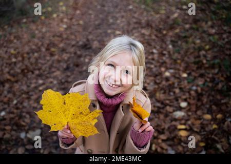 Bonne fille blonde debout avec des feuilles d'érable jaune Banque D'Images