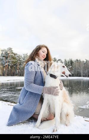 Une femme qui a fait un chien de lévrier devant un lac gelé Banque D'Images