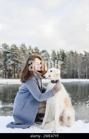 Une femme mature qui a fait un chien de lévrier devant un lac gelé Banque D'Images
