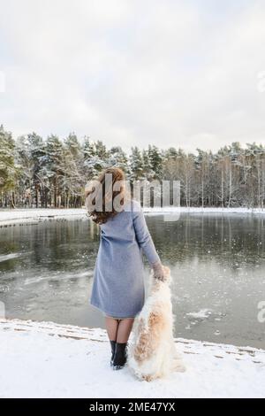 Femme mature debout avec un chien greyhound devant un lac gelé Banque D'Images
