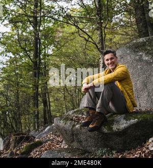 Heureux homme mûr assis sur le rocher dans la forêt Banque D'Images