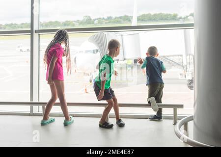 Sœur avec des frères regardant la préparation de l'avion pour l'embarquement depuis la fenêtre du terminal de l'aéroport Banque D'Images