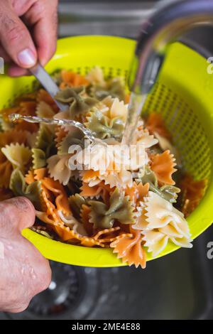 Mains de l'homme laver les pâtes noeud papillon dans l'évier Banque D'Images