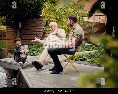 Père, fils et petit-fils assis au bassin du jardin parlant et relaxant Banque D'Images