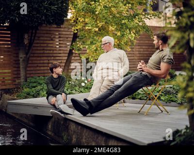 Père, fils et petit-fils assis au bassin du jardin parlant et relaxant Banque D'Images