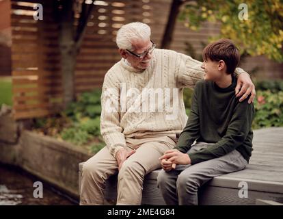 Petit-fils et grand-père assis dans le jardin et parlant ensemble Banque D'Images