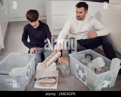 Père et fils séparant les déchets en boîtes de recyclage Banque D'Images