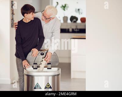 Le grand-père et le petit-fils trient le papier et le plastique dans un bac de tri Banque D'Images