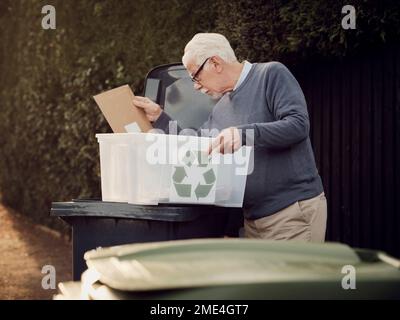 Homme senior plaçant les déchets de recyclage séparés dans la poubelle Banque D'Images