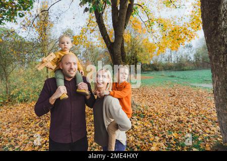 Les parents offrent une promenade en porcgyback aux enfants dans la forêt d'automne Banque D'Images