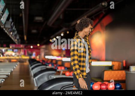 Homme souriant avec main dans les cheveux debout à la piste de bowling Banque D'Images