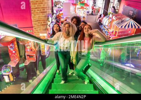 Amis multiraciaux sortant de l'escalier mécanique dans une salle de jeux Banque D'Images