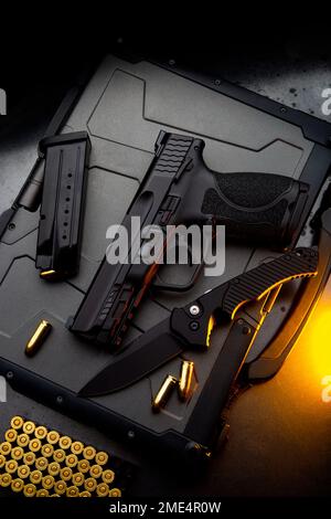 Un pistolet, des cartouches pour lui et un couteau pliant sur un fond sombre. Kit d'auto-défense et de survie. Armes à feu et armes à feu à bordure compacte. Banque D'Images