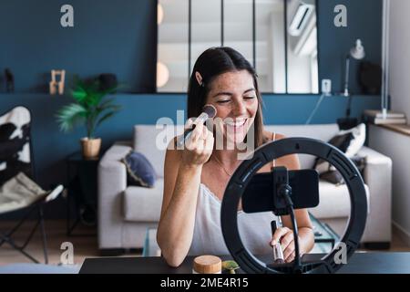 Joyeux tutoriel sur l'enregistrement de maquillage d'influenceur sur smartphone à la maison Banque D'Images