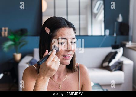 Jeune femme appliquant du maquillage sur le visage à la maison Banque D'Images