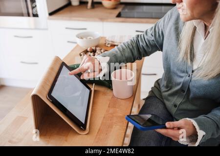 Femme utilisant un PC tablette assis à une table dans la cuisine Banque D'Images