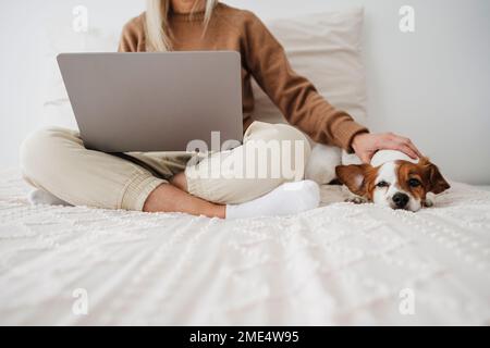 Femme utilisant un ordinateur portable et chien de course sur le lit Banque D'Images