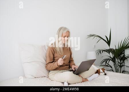 Femme mûre souriante payant avec une carte de crédit sur un ordinateur portable à la maison Banque D'Images