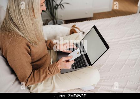 Femme d'âge mûr payant avec carte de crédit par ordinateur portable dans la chambre Banque D'Images