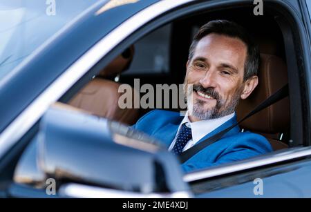 Homme d'affaires souriant et mûr à la recherche d'un miroir latéral de voiture Banque D'Images