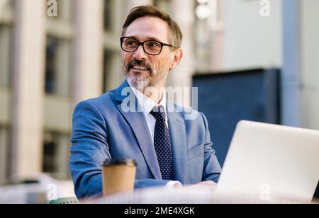 Femme mûre et attentionnés assise devant un ordinateur portable au café Banque D'Images