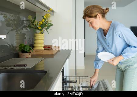 Femme chargeant des plaques dans le lave-vaisselle dans la cuisine à la maison Banque D'Images