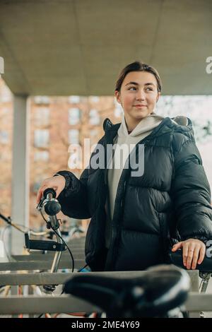 Adolescente souriante en veste noire debout à la station de stationnement pour vélos Banque D'Images