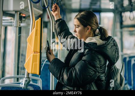 Une adolescente achète son billet via un smartphone en tram Banque D'Images