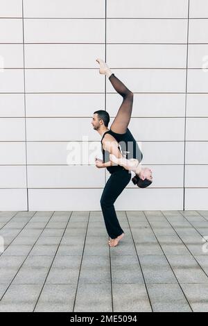 Homme soulevant une jeune femme à l'envers devant le mur Banque D'Images