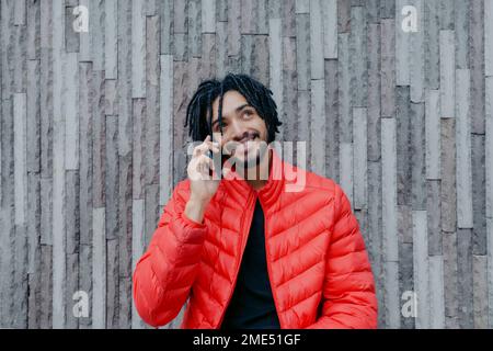 Un homme heureux qui parle sur un smartphone devant le mur Banque D'Images