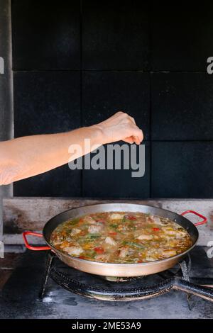 Femme arrosé de assaisonnements sur la paella dans la cuisine extérieure Banque D'Images