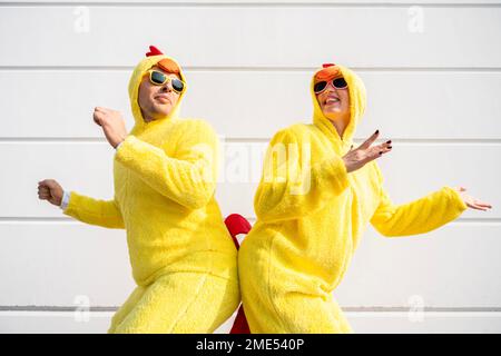 Femme et homme heureux portant des costumes de poulet jaune ayant du plaisir devant le mur Banque D'Images