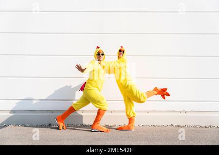 Joueur homme et femme portant des costumes de poulet s'amusant devant le mur Banque D'Images