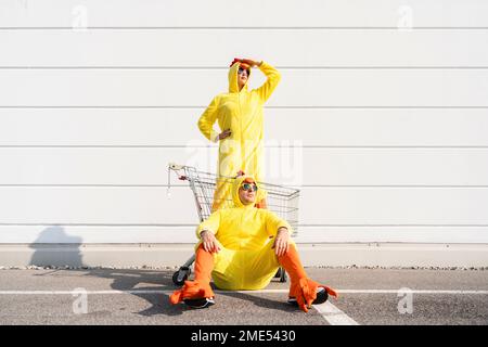 Homme devant une femme portant des yeux de protection de costume de poulet jaune dans le chariot Banque D'Images