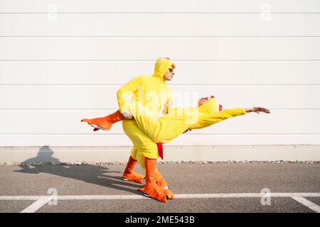 Homme heureux avec une femme portant des costumes de poulet et dansant devant le mur Banque D'Images