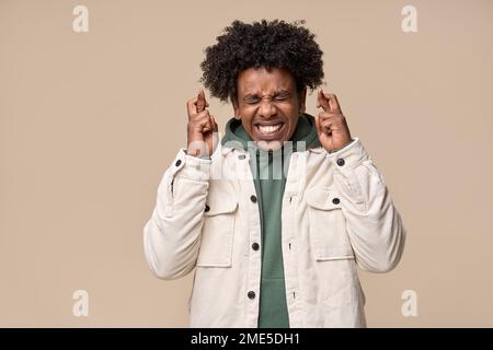 Un jeune homme afro-américain nerveux croisant les doigts et faisant des souhaits, mendiant pour la chance. Banque D'Images